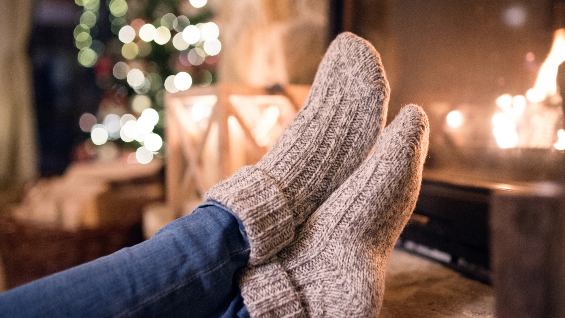 Photo de deux pieds en chaussettes devant un sapin de Noël. 