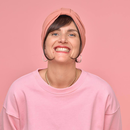 Photo de Sabine qui porte un bonnet et un pull rose, avec une peine de créoles.