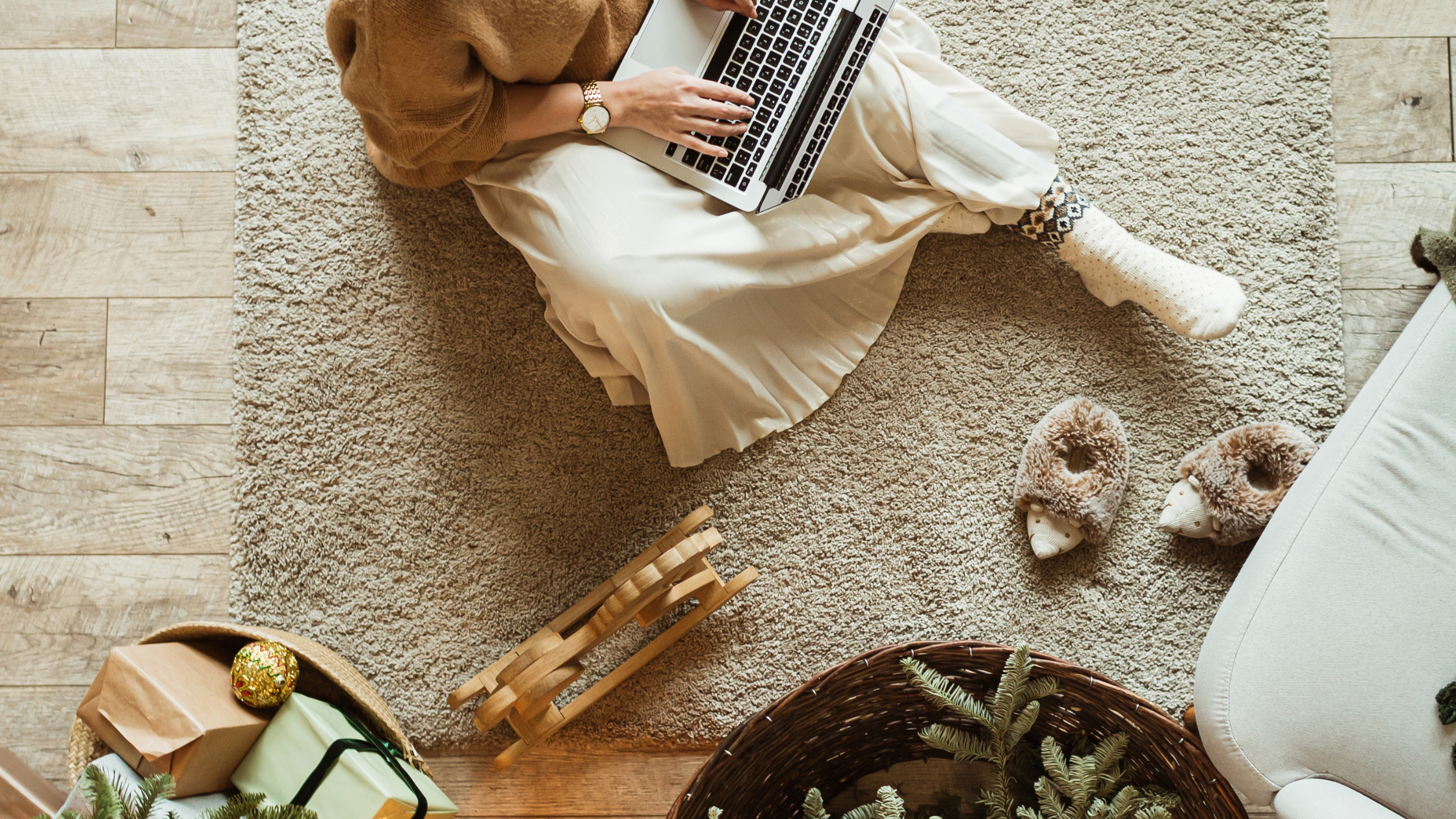 Photo d'une femme assise sur le tapis de son salon, en train de travailler sur son ordinateur. 